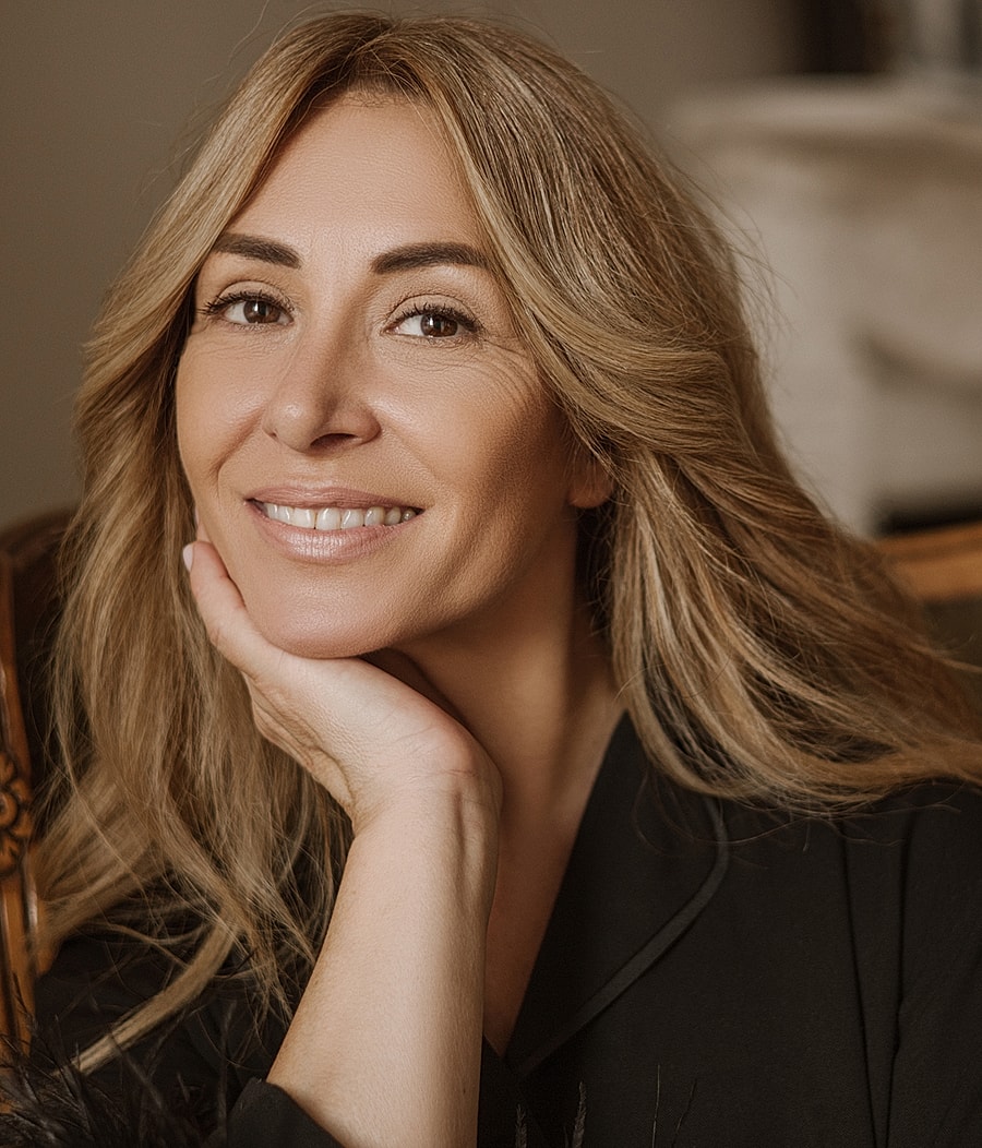 Smiling Melbourne facial cosmetic surgery model with long hair and hand under chin.